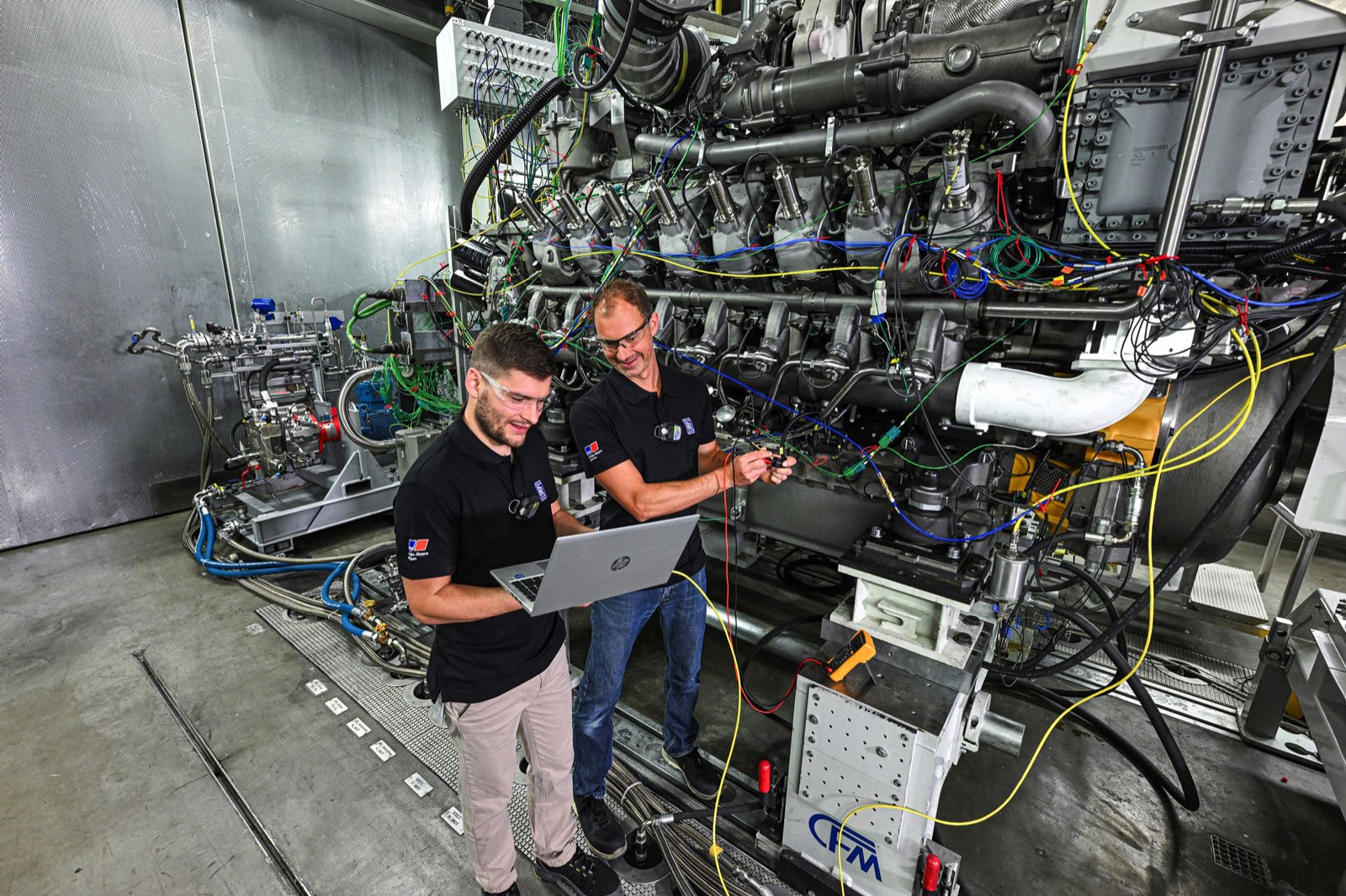 © Rolls-Royce Power Systems Two engineers reviewing test data beside an mtu methanol engine on a Rolls-Royce Power Systems test bed